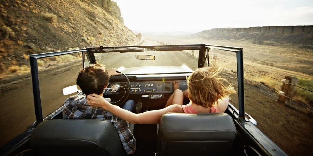 Young couple driving convertible at sunset